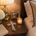 Cross with decorative elements next to a candle and aframed photo on a wooden surface