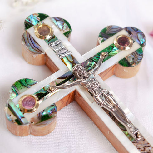 Eastern olive wood cross with crucifix, white and green Mother of Pearl decor, lying on white background with petals.