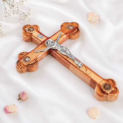 Large handmade budded olive wood cross with silver crucifix lying flat on white background with rose petals.