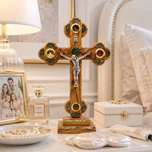 Decorative cross with religious figure, Chanel perfume bottle, and jewelry on a table.