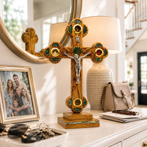 Decorative cross with green gemstones on a table with a lamp and family photo in the background