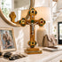 Decorative cross with green gemstones on a table with a lamp and family photo in the background