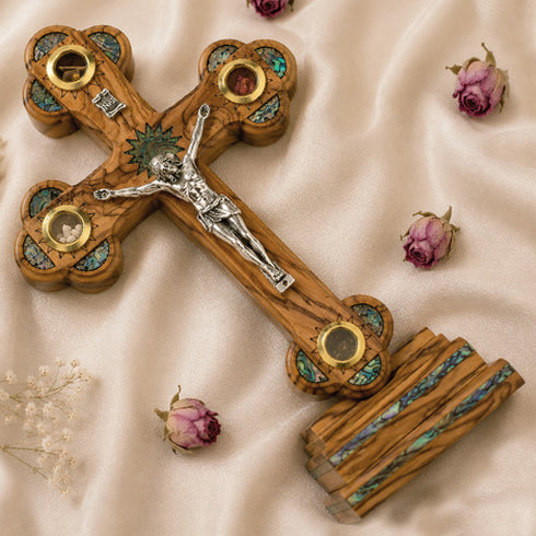 Wooden cross with intricate designs and a figure on a beige fabric background with dried flowers.