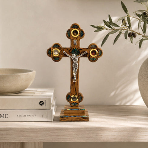 Decorative standing wooden cross with intricate designs on a shelf with books and a plant.