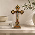 Decorative standing wooden cross with intricate designs on a shelf with books and a plant.