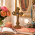 Religious setting with cross, candle, flowers, and statue of a religious figure.