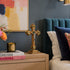 Decorative cross on a nightstand with books and a candle, against a blue wall with abstract art.