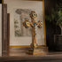 Decorative cross with gold and green accents on a wooden surface, with books and a framed picture in the background.
