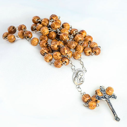 Packshot of carved olive wood rosary with silver Mary emblem centerpiece and silver crucifix.