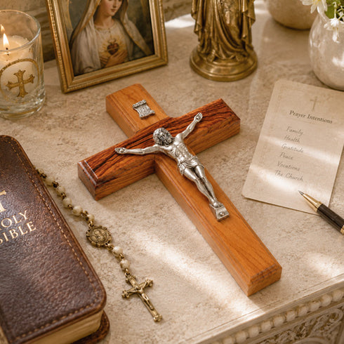 Wooden cross with Jesus Christ figure, Bible, rosary, and prayer paper on a table.