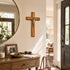 Wooden cross on a wall above a wooden console table with decor items.