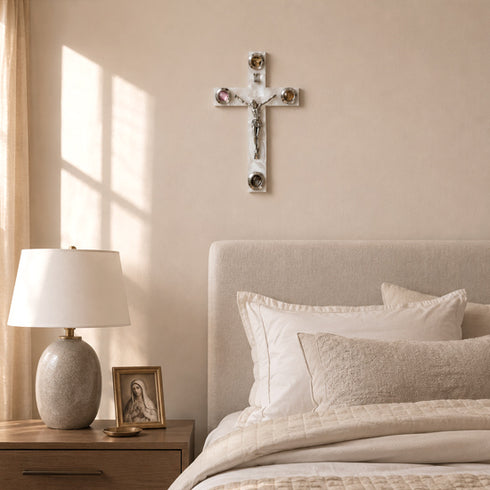 Neatly made bed with pillows, lamp, and crucifix on a wall in a bedroom.