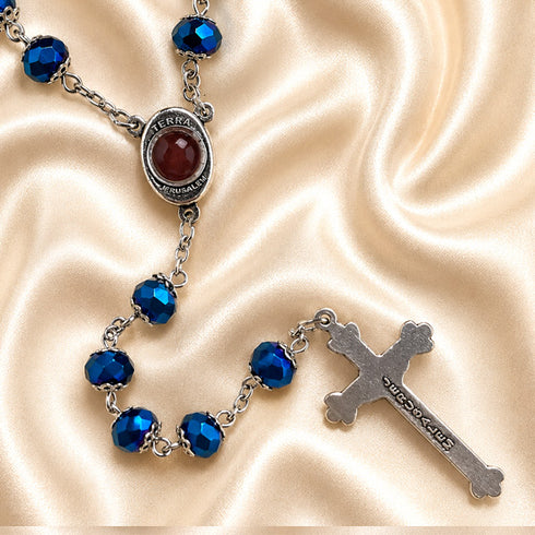 Blue crystal rosary with faceted beads, Jerusalem holy soil centerpiece and silver crucifix on champagne satin.