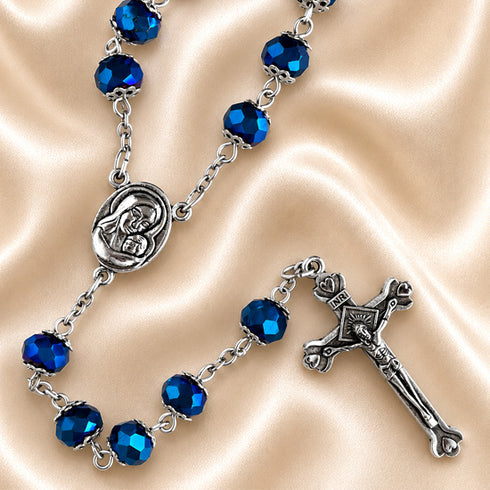 Blue crystal rosary with silver-tone Virgin Mary centerpiece and ornate crucifix displayed on champagne satin.
