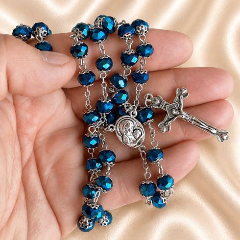 Dark blue crystal rosary with faceted beads, Virgin Mary centerpiece and ornate silver crucifix displayed in a hand.