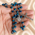 Dark blue crystal rosary with faceted beads, Virgin Mary centerpiece and ornate silver crucifix displayed in a hand.