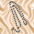 Blue crystal rosary with faceted beads, Jerusalem holy soil centerpiece and silver crucifix displayed on champagne satin.