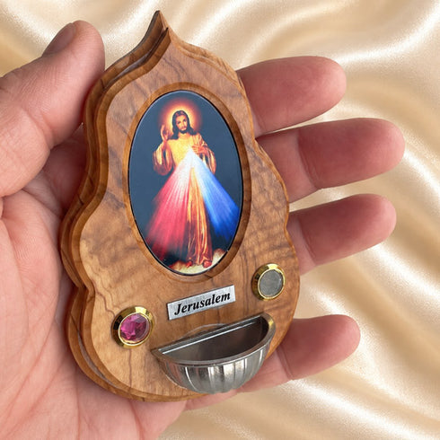 Hand holding a Divine Mercy olive wood holy water font, showing its small size and devotional details