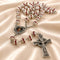 Silver rosary with red and clear beads, a silver crucifix, and a central medallion, on a beige satin fabric background.