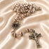 A silver-toned rosary with red enamel accents and a crucifix pendant, displayed on draped cream satin fabric.
