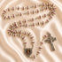 Silver rosary with red and white beads, a heart-shaped pendant and a silver crucifix, on a beige satin fabric background.