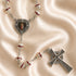Silver rosary with red enamel beads and a central medallion featuring a religious image, on a beige fabric background.