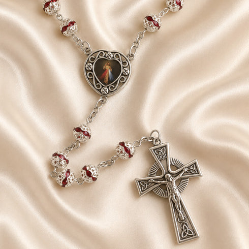 A silver rosary with red and clear beads, a medallion featuring a religious image, and a detailed crucifix pendant.