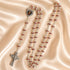 A silver rosary with red beads and a heart-shaped centerpiece, on a beige satin fabric background.