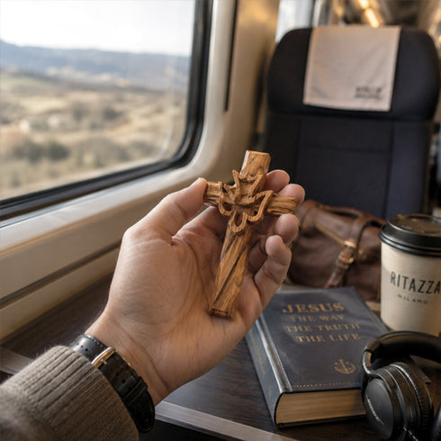 Hand holding a wooden cross with a book and coffee cup on a train table