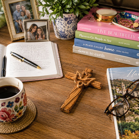 Desk with books, a cross, a cup of coffee, and a notebook.