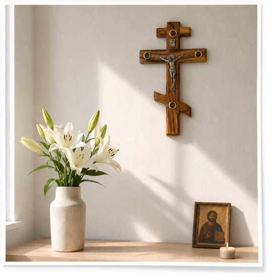 Wooden cross, vase with white lilies, and framed picture on a shelf against a light wall.