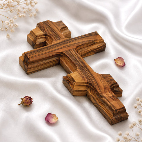 Wooden cross on a white fabric background with dried flowers.