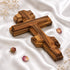 Wooden cross on a white fabric background with dried flowers.