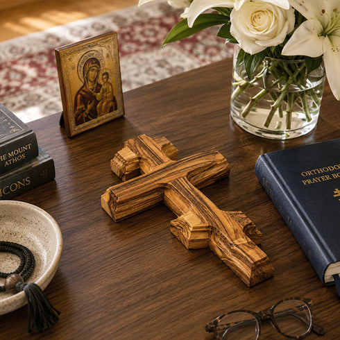 Wooden cross, Orthodox prayer book, and vase with flowers on a wooden surface.
