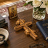 Wooden cross, Orthodox prayer book, and vase with flowers on a wooden surface.