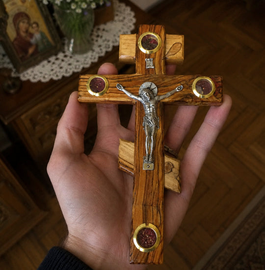 Wooden cross with a figure of Jesus held in a hand, with a blurred background