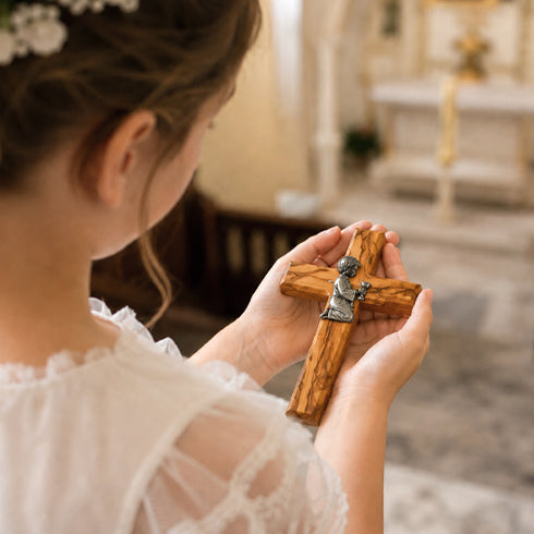 Girl holding a wooden cross with a small figurine in a church setting
