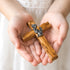 Wooden cross held in a child's hands against a light background