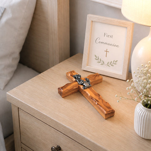 Wooden cross on a nightstand with a 'First Communion' frame in the background