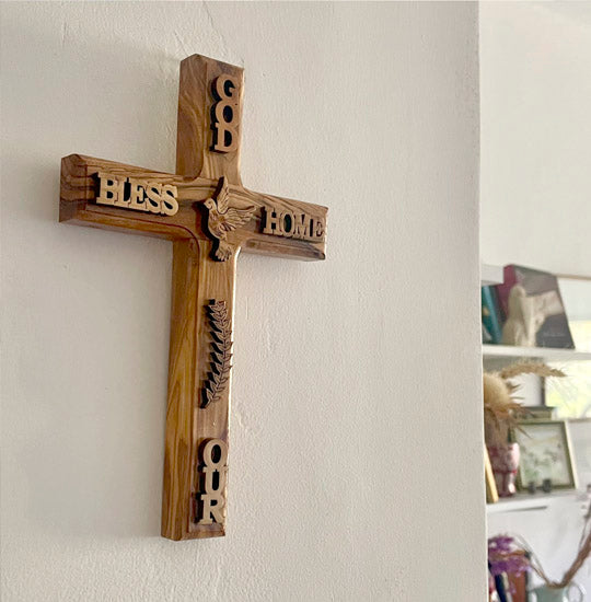Large latin olive wood cross with "God Bless Our Home" and a dove engraved, hanging on the wall.