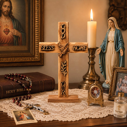 Wooden cross with engraved words, lit candle, religious statues, and books on a table.