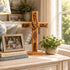 Wooden cross with engraved text on a table with books and a family photo