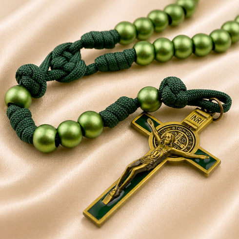 A green rosary with a dark green knotted cord, and a gold-toned crucifix with green accents, on a satin beige fabric.