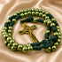 A rosary with green beads, dark green cord, and a gold-tone St Benedict crucifix, on a beige satin fabric.