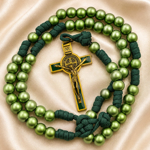 A green rosary with dark green cord and a gold-toned crucifix, on a beige satin background.