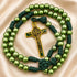 A green rosary with dark green cord and a gold-toned crucifix, on a beige satin background.