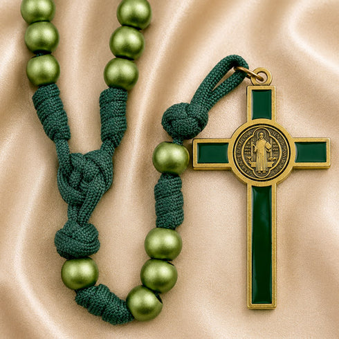 A green and gold rosary with green beads and a green cross pendant, displayed on a beige satin fabric background.