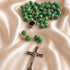 A green faceted bead rosary with a silver-tone crucifix and centerpiece, arranged on draped satin fabric.