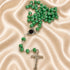 A green rosary with a silver-tone cross pendant engraved with 'JESUS', on a draped beige satin fabric background.