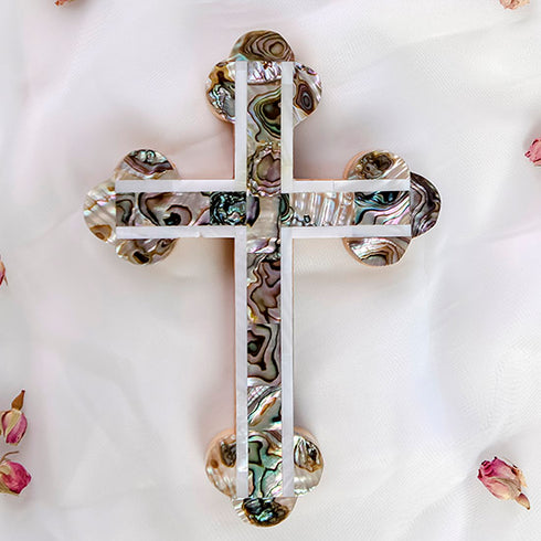 Frontal image of a handcrafted budded olive wood cross with green-white mother of pearl accents, placed on a white background with rose petals beside it.